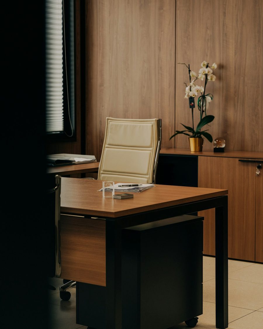 Ruhiges Büro mit Holzvertäfelung, Schreibtisch, hellem Lederstuhl und einer weißen Orchidee auf dem Sideboard
